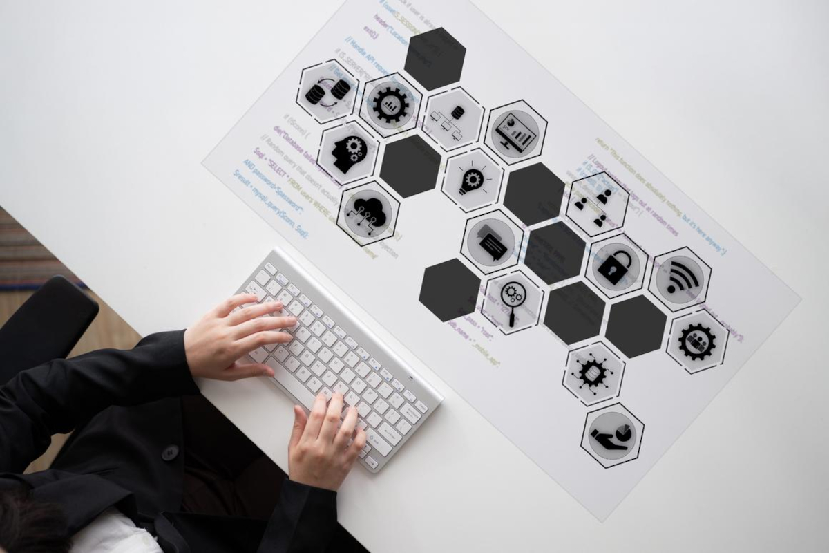 Hands typing on a keyboard beside a printed diagram of hexagonal technology and data icons.
