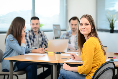 Four colleagues collaborating around a table with a laptop in a bright meeting room.